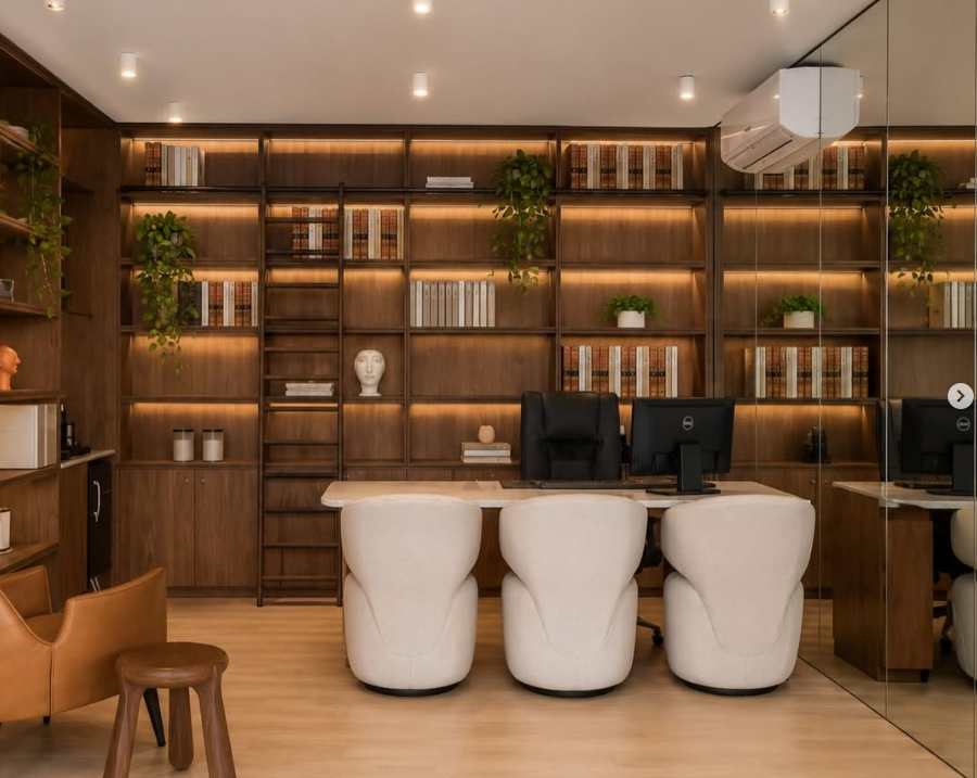 Escritório com estante iluminada, mesa e três poltronas